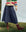 A person in a striped sweater and brown lace-up boots stands gracefully on the grass, wearing THE GREAT. PS25's The Rhythm Skirt in Riverside Blue that sways with every step.