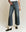 Person wearing ultrahigh-waisted, wide-leg jeans from THE GREAT. PF24's The Seafair Jean in Marina Wash and black shoes, standing against a plain background.