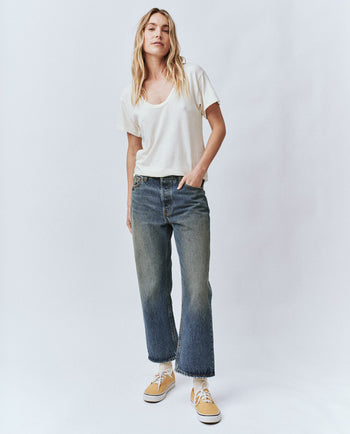 woman wearing a scoop neck white tee and medium wash denim pants.